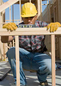 Photo shows carpenter at worksite using a level to check a header.