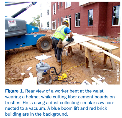 Figure 1: Rear view of a worker bent at the waist wearing a helmet while cutting fiber cement boards on trestles. He is using a dust collecting circular saw con¬nected to a vacuum. A blue boom lift and red brick building are in the background.