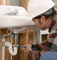 Photo shows plumber tightening a connection during a toilet installation.