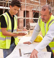 Photo shows two workers reviewing project plans at a construction site.