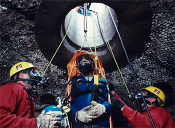 Men extracting a worker from a confined space, all with respirators on